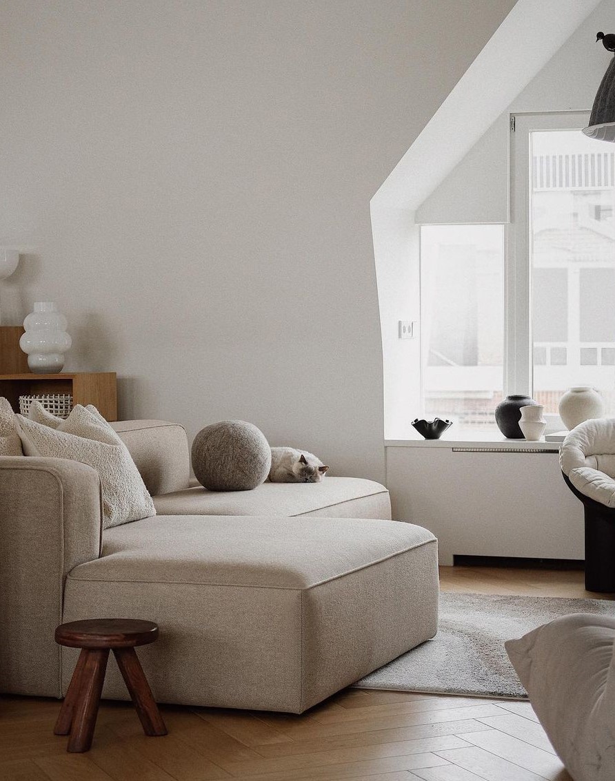 Décoration minimaliste d'un salon avec un pouf rond gris en laine feutrée posé sur un canapé d'angle gris clair