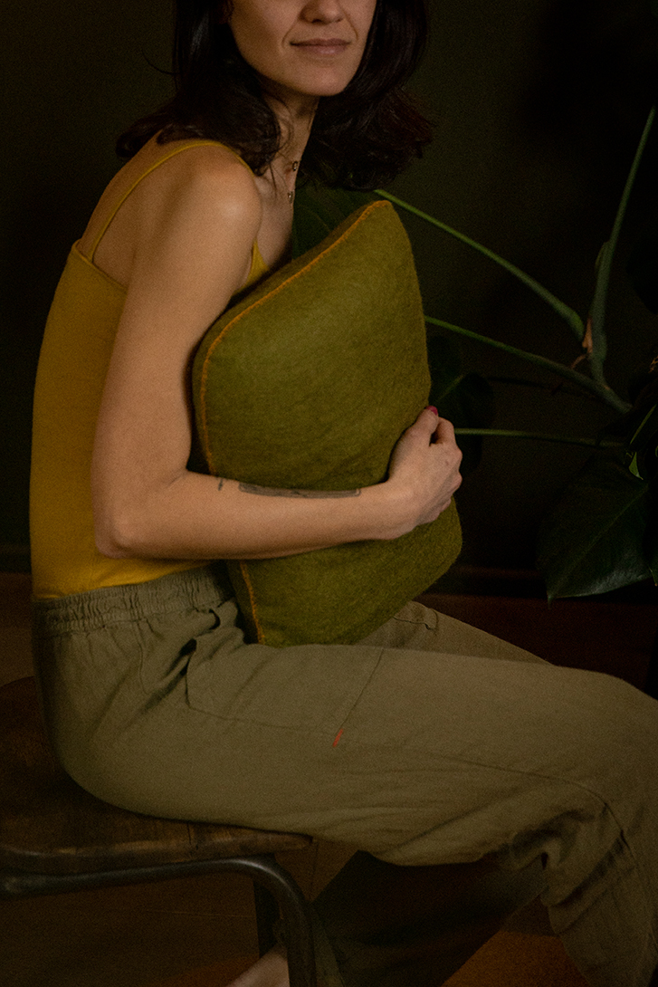 Une femme tenant dans ses bras un coussin rectangulaire en laine feutrée vert