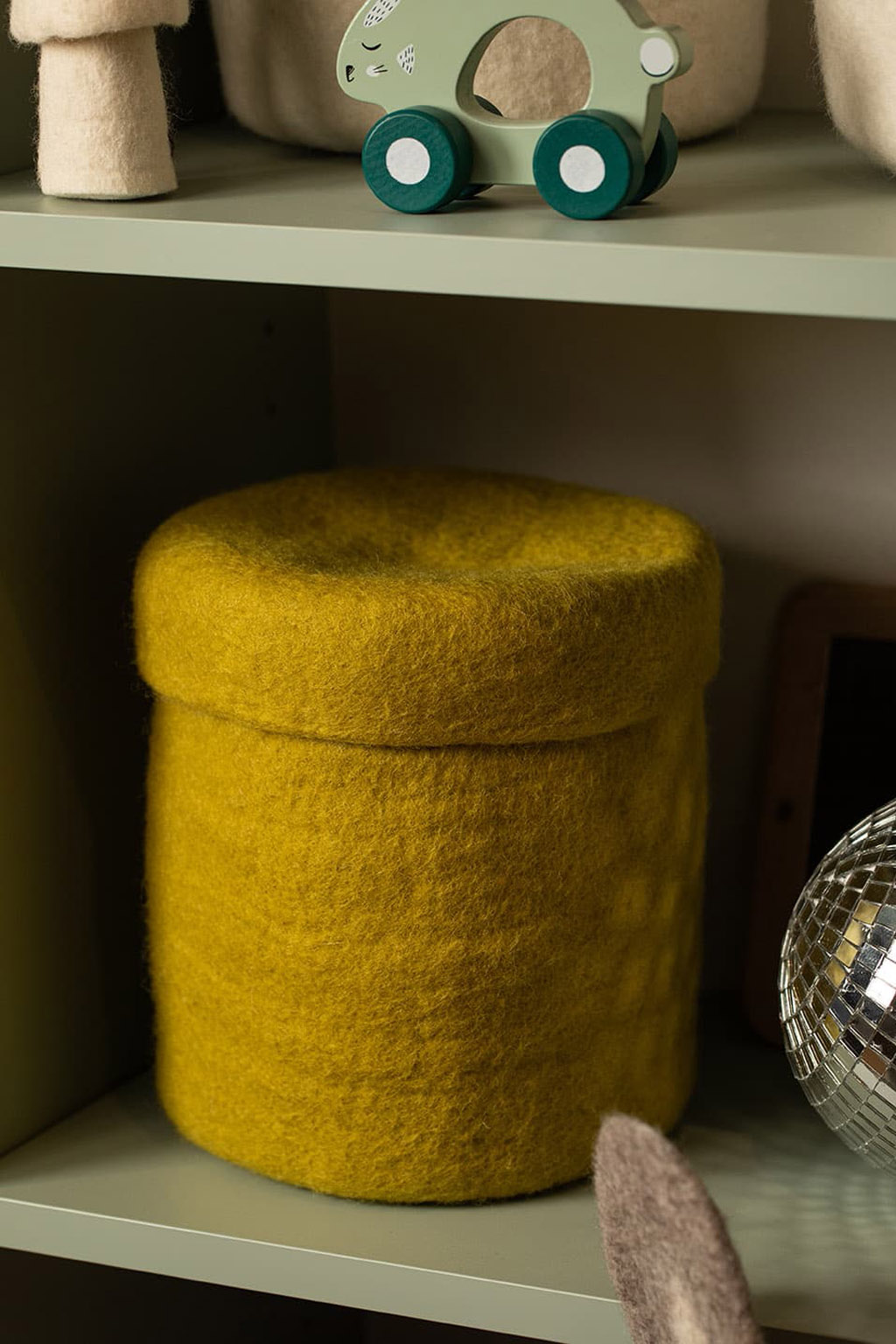 Boite de rangement en feutre de laine verte, de forme ronde, disposée dans une armoire