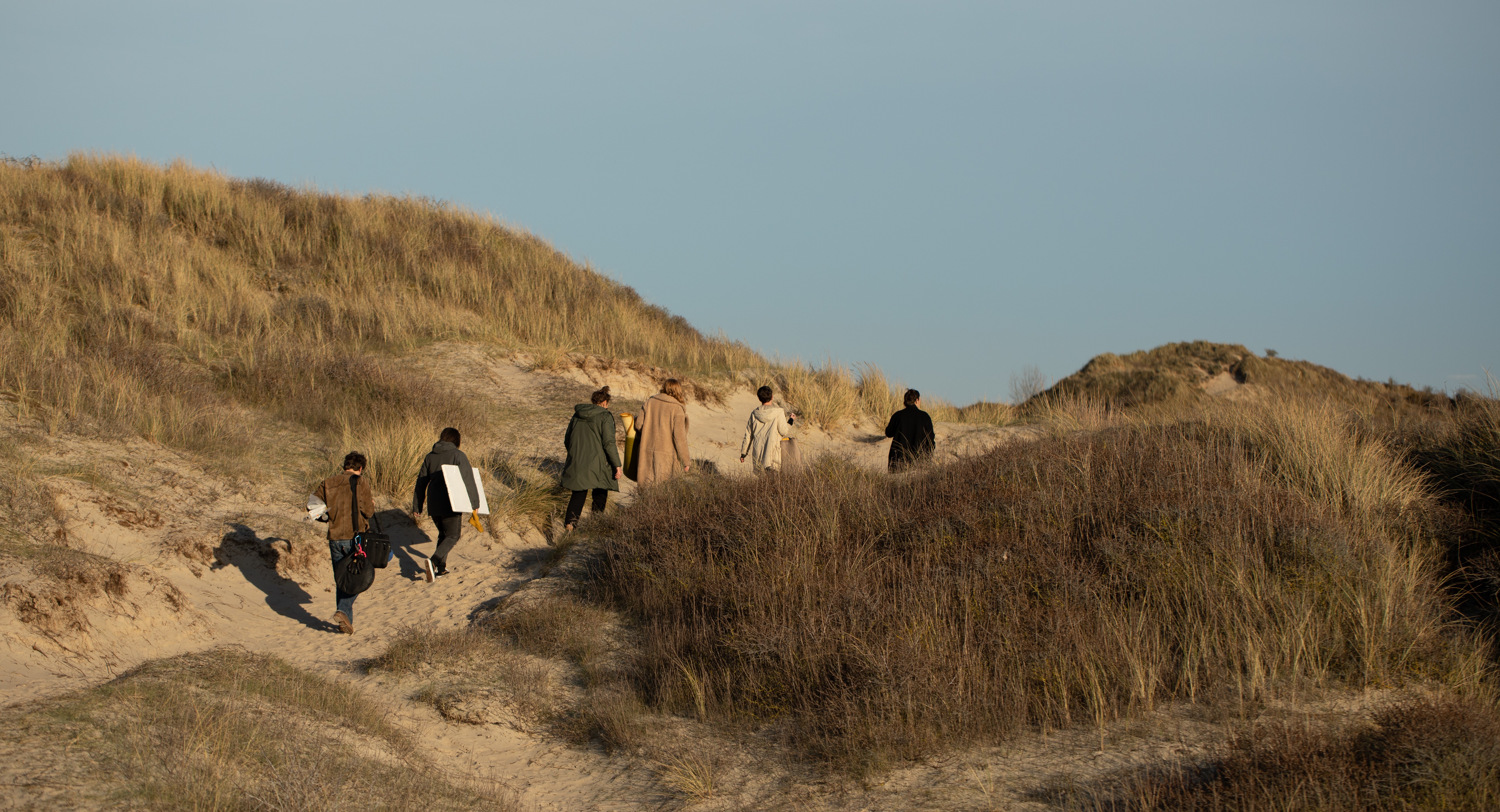 6 personnes de dos marchant dans les dunes
