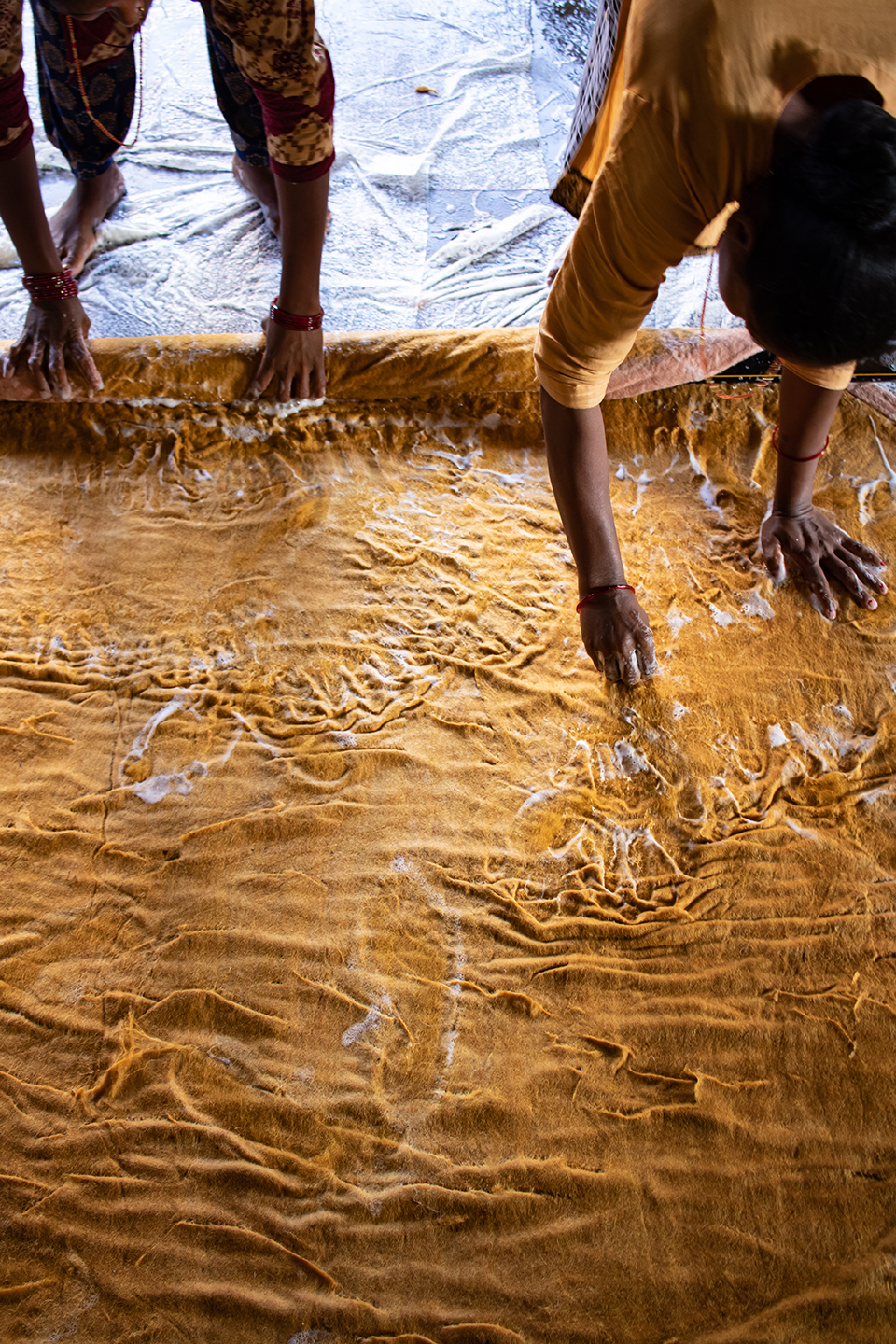 2 femmes népalaises en train de fabriquer un tapis en feutre jaune avec de la laine, de l'eau et du savon