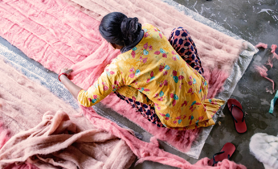 Artisane népalaise en train d'apposer les couches de laine rose pour faire un tapis en feutre