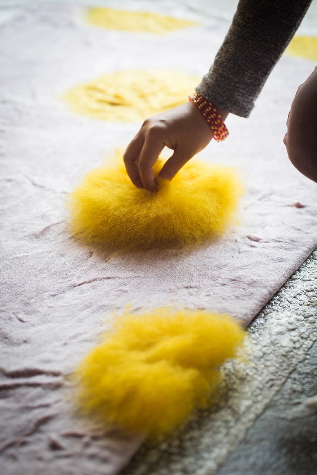 Une artisane qui dépose de la laine pour fabriquer un tapis en feutre