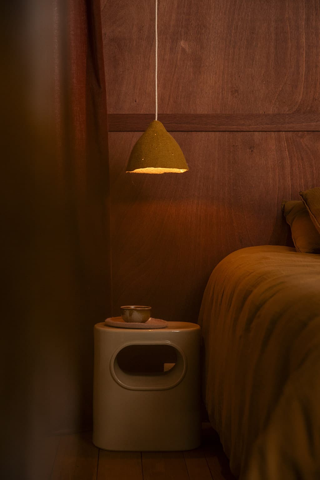Okerkleurige conische lampenkap van wol voor een houten hoofdeinde, als verlichting van een nachtkastje