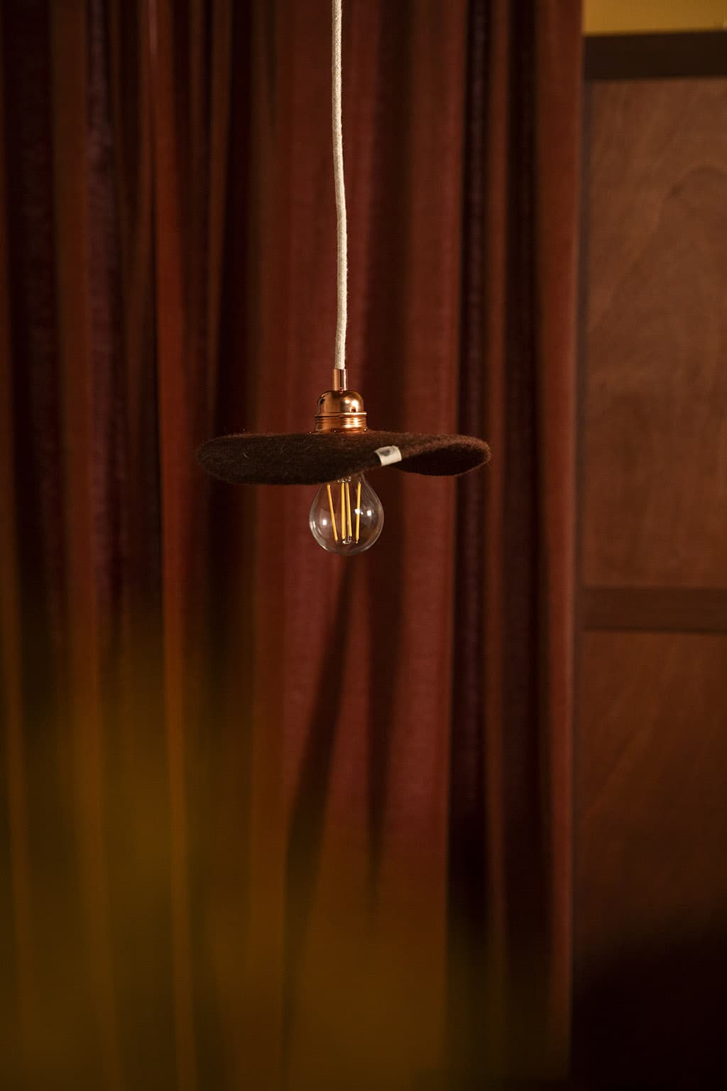 Platte bruine hanglamp van wolvilt voor de verlichting van een nachtkastje