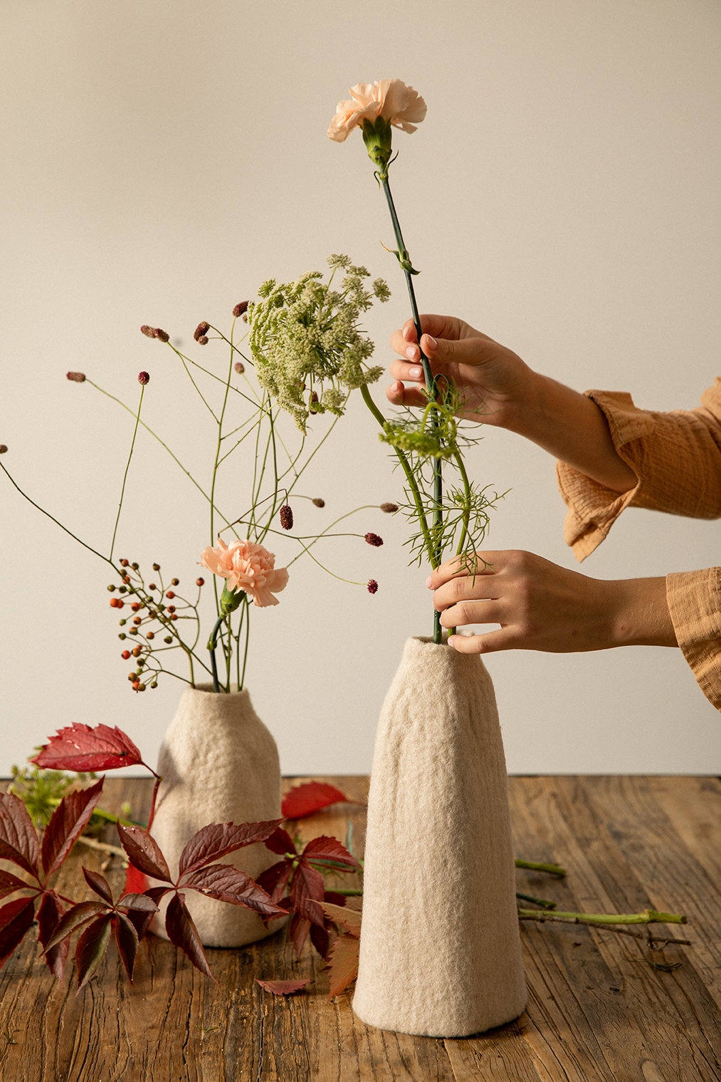 Femme glissant quelques fleurs dans deux vases en feutre de laine