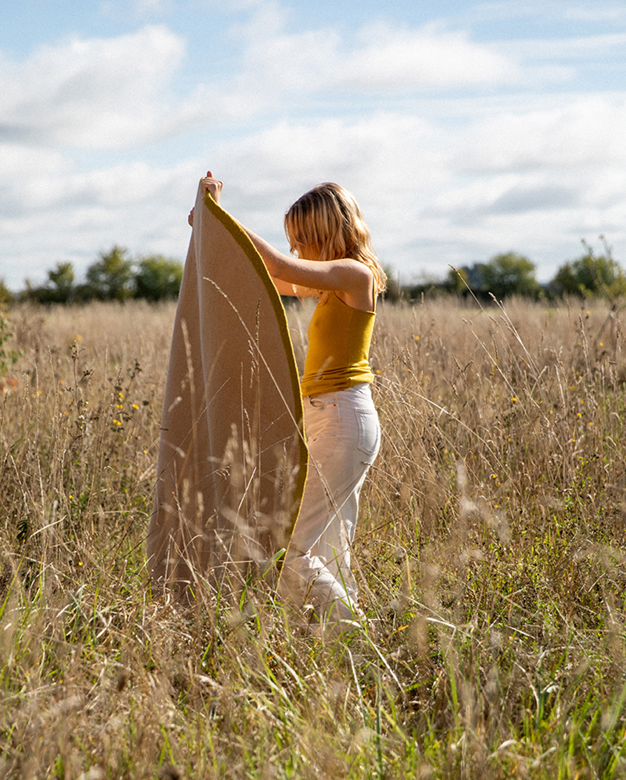 Woman carrying a round wool felt carpet in a field
