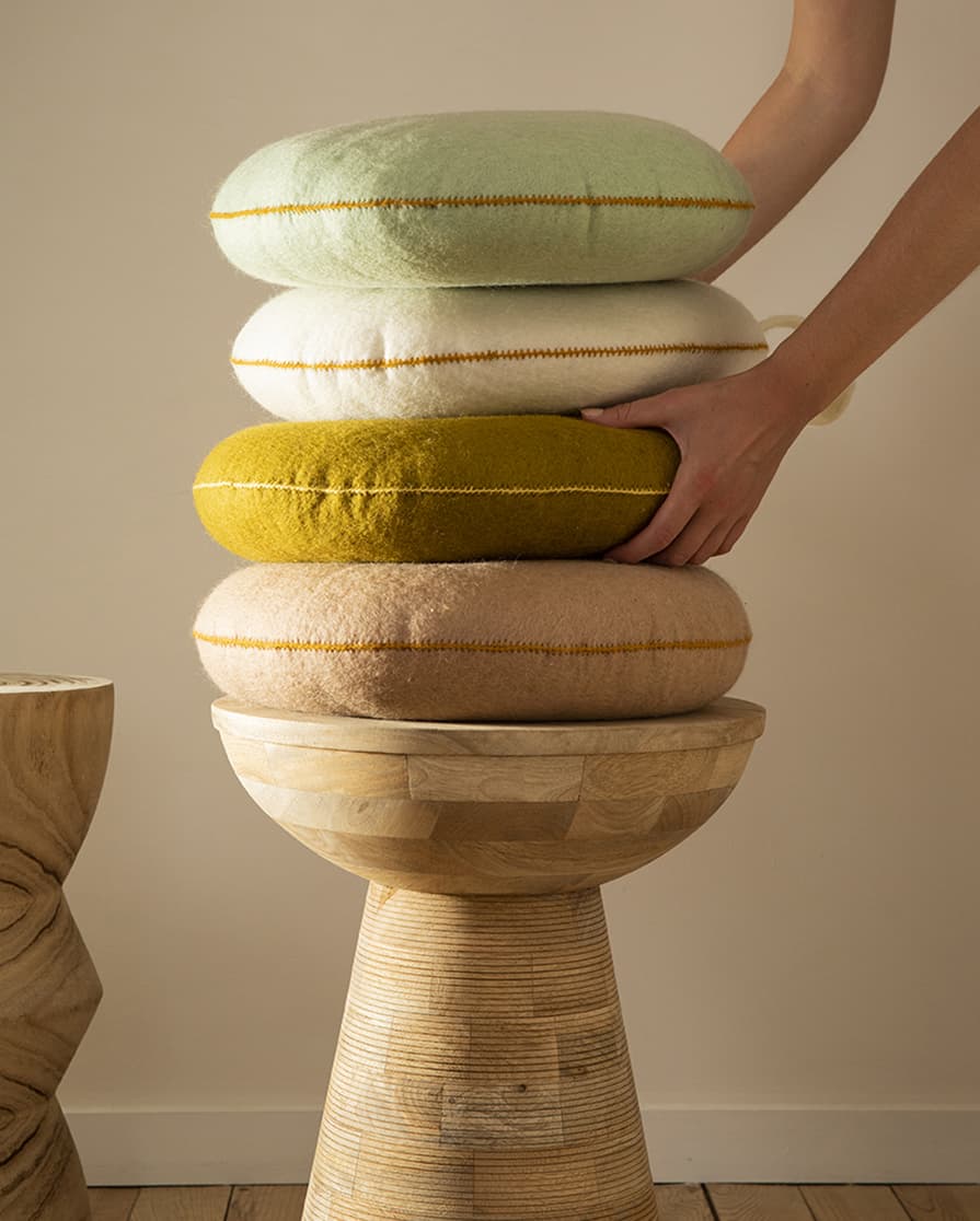 Pile de 4 coussins en feutre de laine posés sur un tabouret en bois