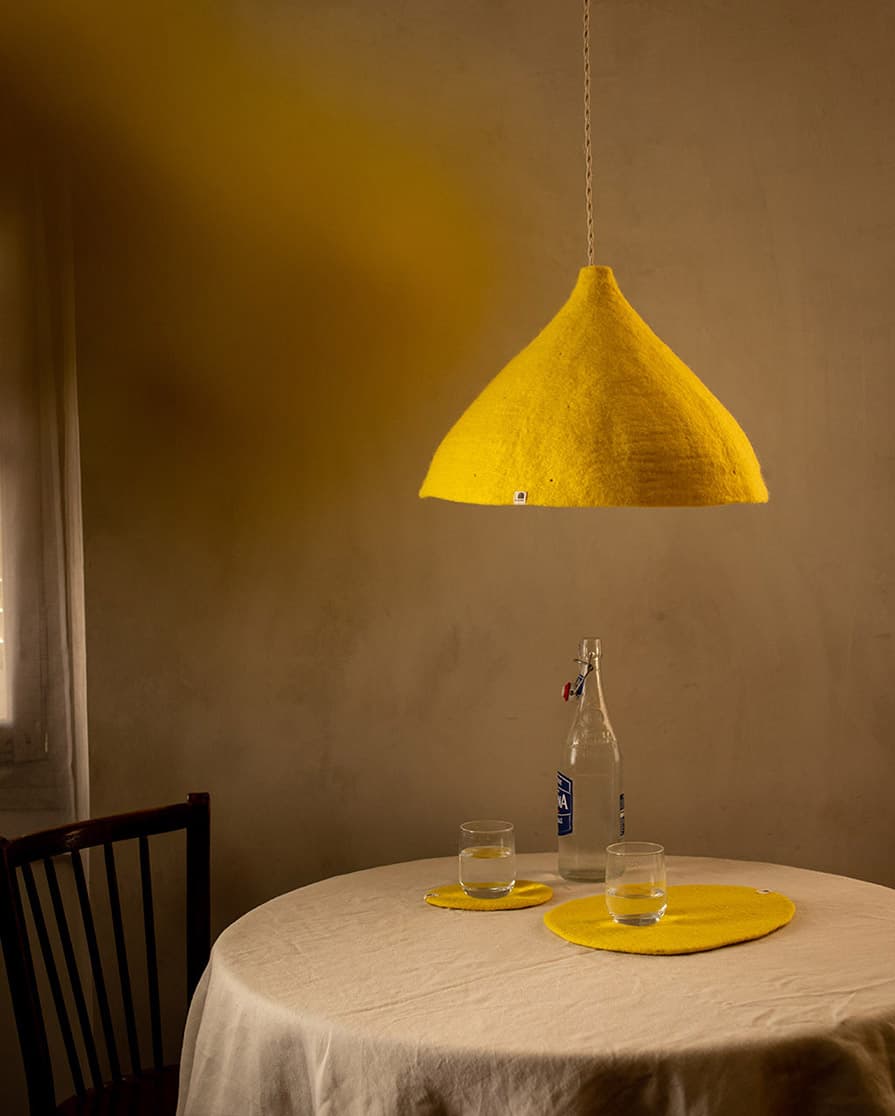 Abat-jour conique jaune citron en feutre de laine suspendu au-dessus d’une table à manger