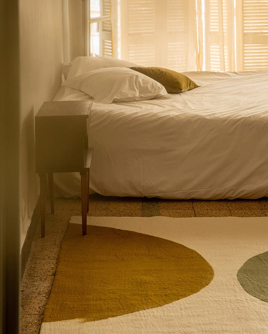 Tapis rectangulaire en laine feutrée vert et blanc au pied d’un lit dans une chambre parentale