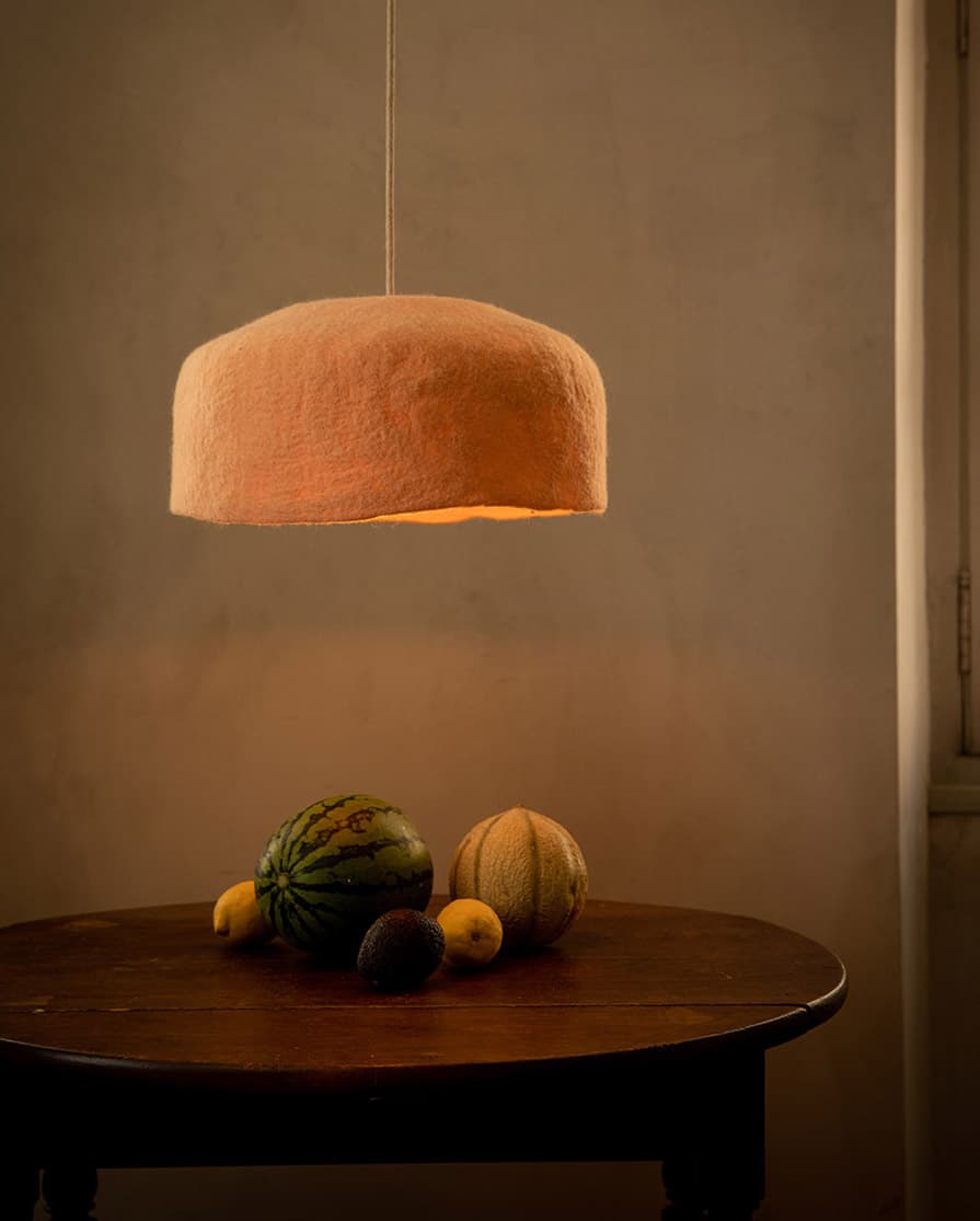 Large organic-style pink and white felted wool lampshade hanging above a round wooden dining table