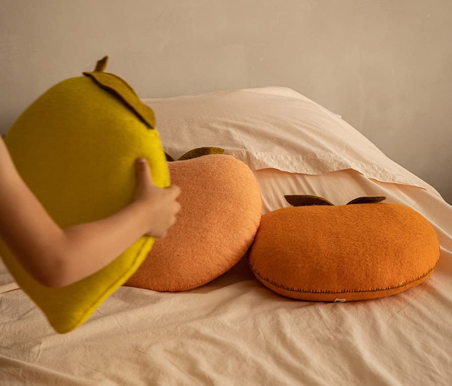 Dekorative Kissen aus gefilzter Wolle mit Fruchtformen auf einem Bett.