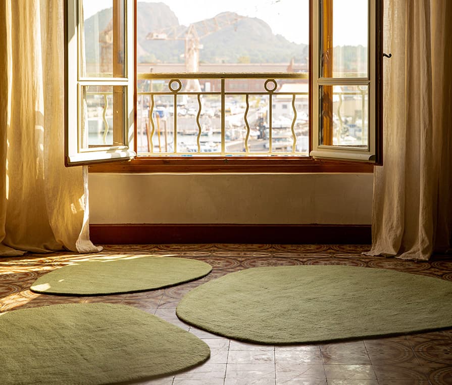 Trio de petits tapis de forme organique en laine feutrée couleur vert sauge sur un carrelage ancien