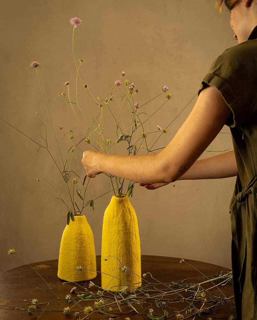 Duo de cache-vases jaunes en laine feutrée sur une table en bois