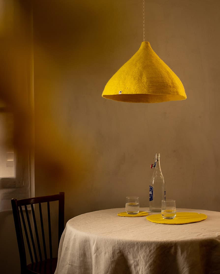 Abat-jour conique jaune en laine feutrée suspendu au-dessus d’une table à manger ronde