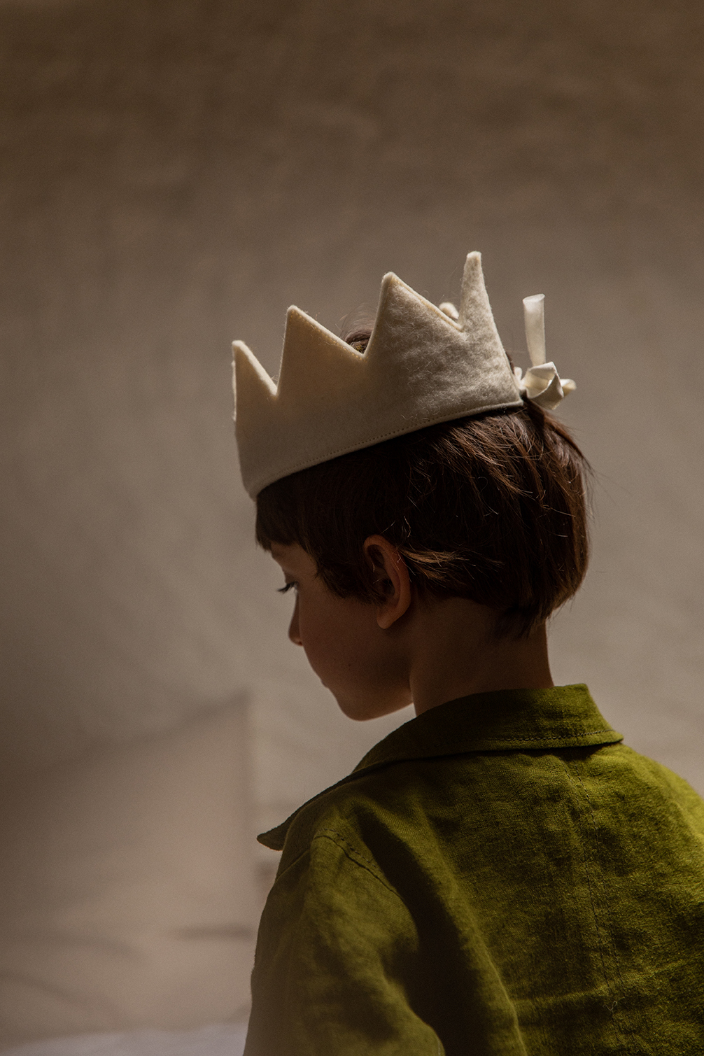 Little boy from the back with a white felt crown on his head