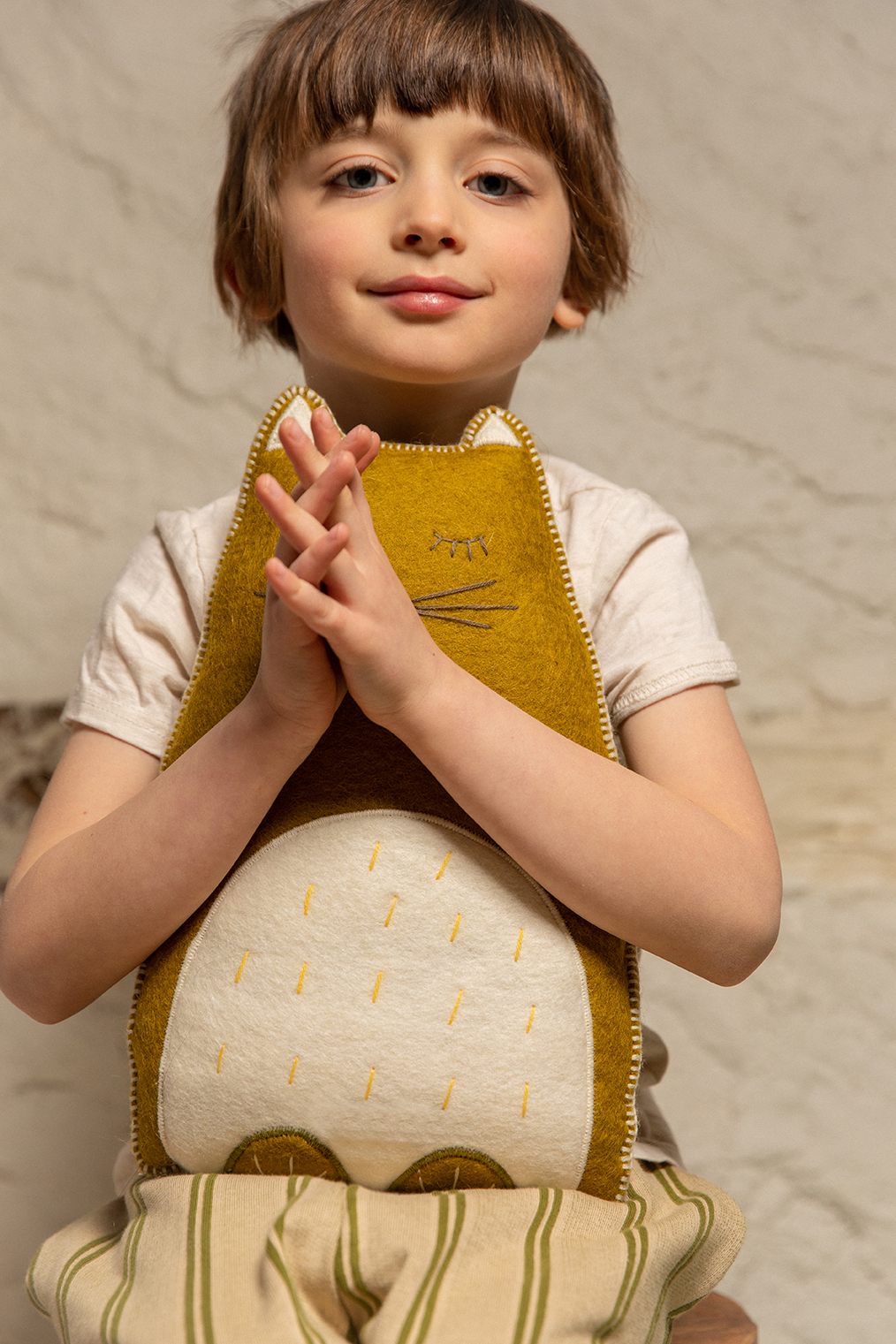 Little boy hugging a green wool felt cat cushion