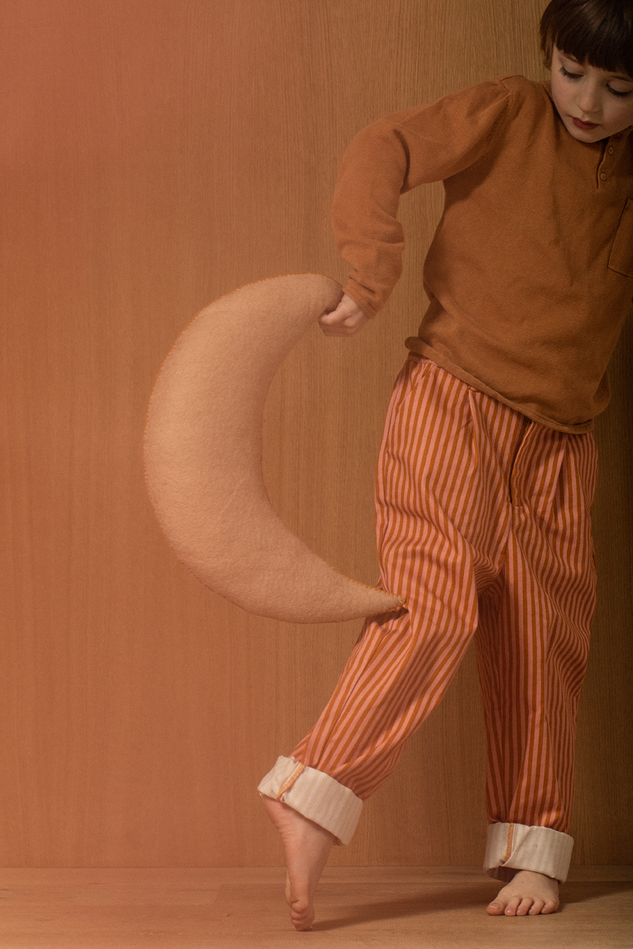 Little boy holding a felted wool pink crescent moon cushion