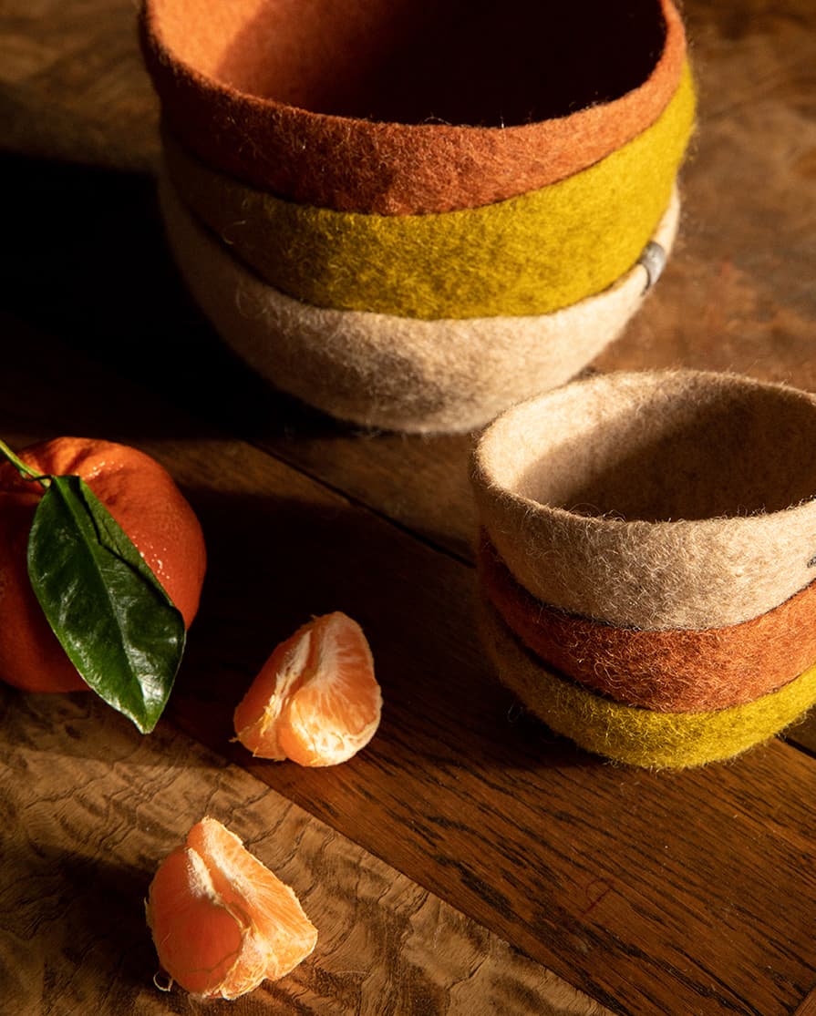 2 stacks of 3 large and 3 small green, pink and red wool felt bowls on a wooden table