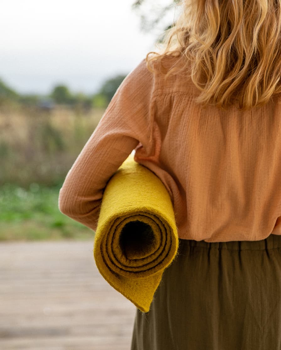 Femme de dos portant un tapis roulé sous le bras