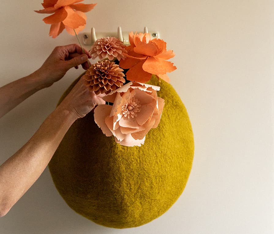 Woman slipping paper flowers into a green wool felt storage basket hung on the wall