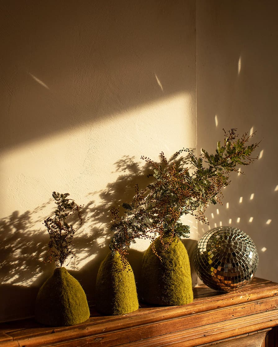 Trio de soliflores verts en feutre de laine disposés sur le rebord du manteau de la cheminée
