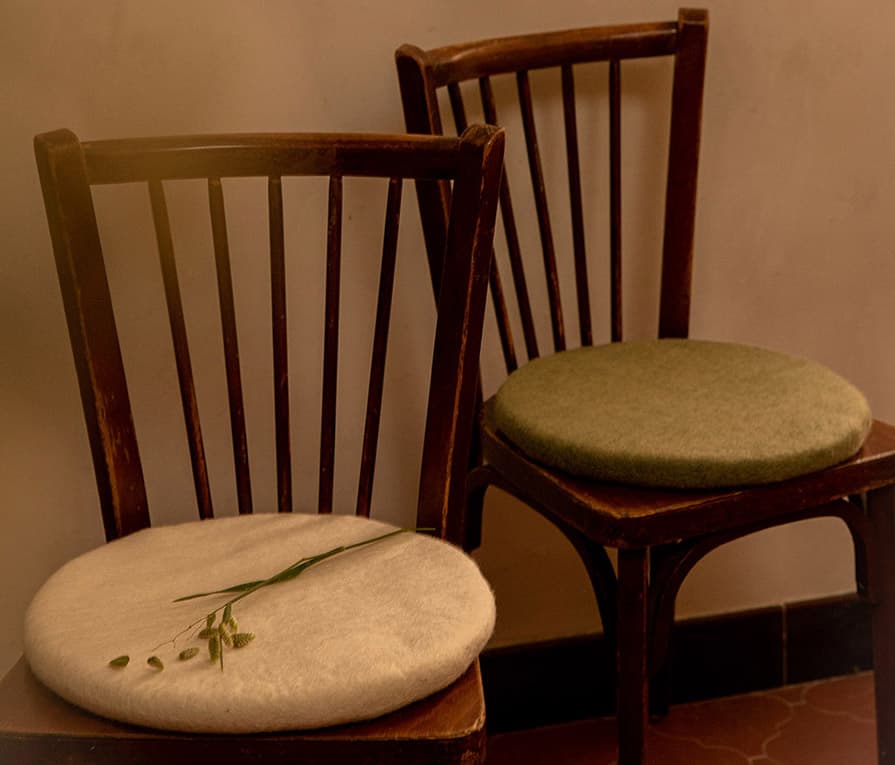 Galettes de chaise blanche et vert sauge en laine sur des chaises en bois