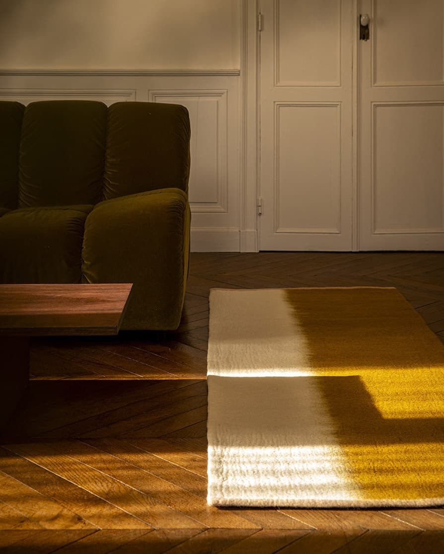Lang rechthoekig driekleurig wollen vloerkleed aan het voeteneinde van een fluwelen bank en een houten tafel