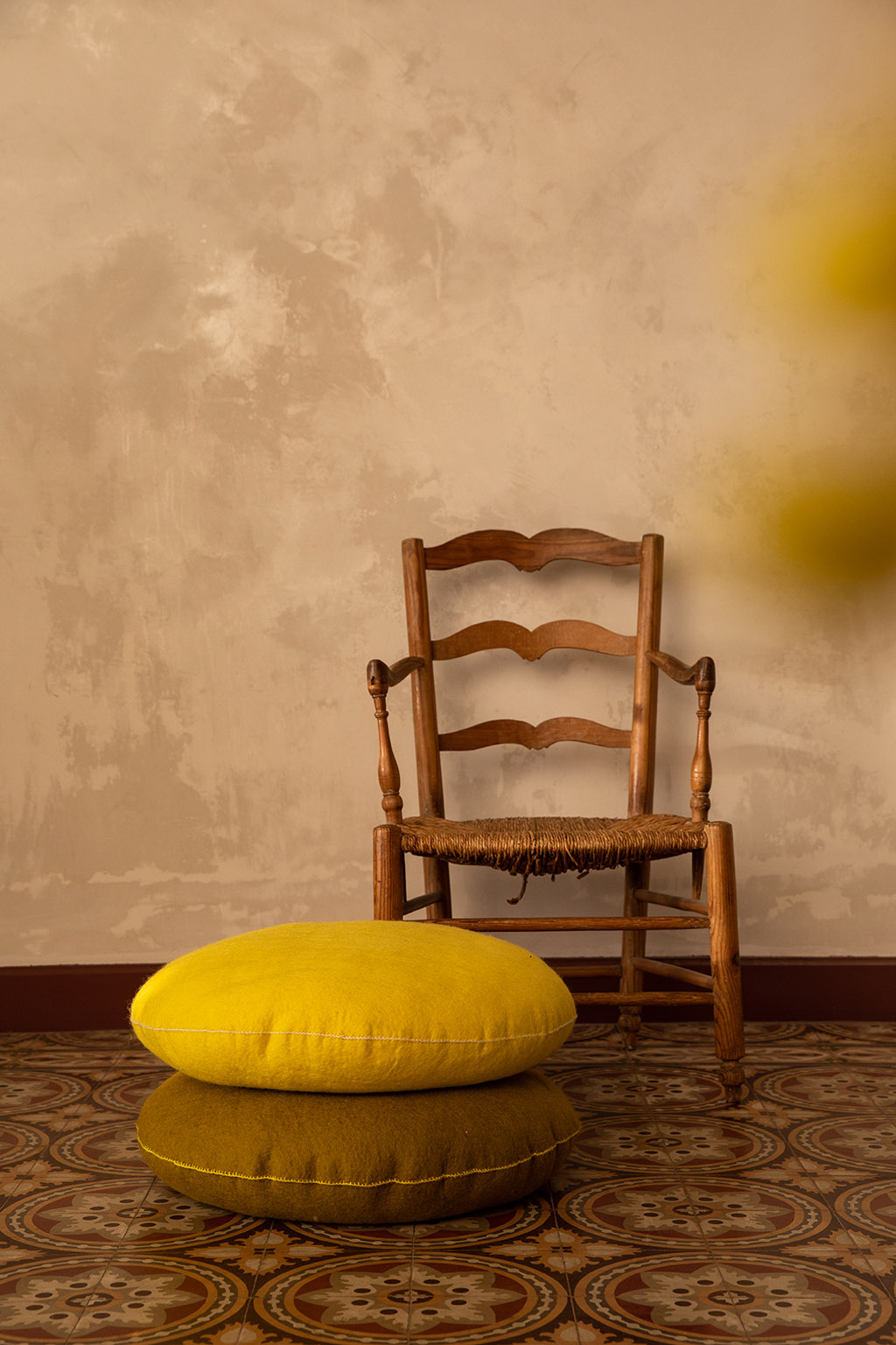 Chaise en bois et coussins ronds en feutre posés sur un sol carrelé ancien